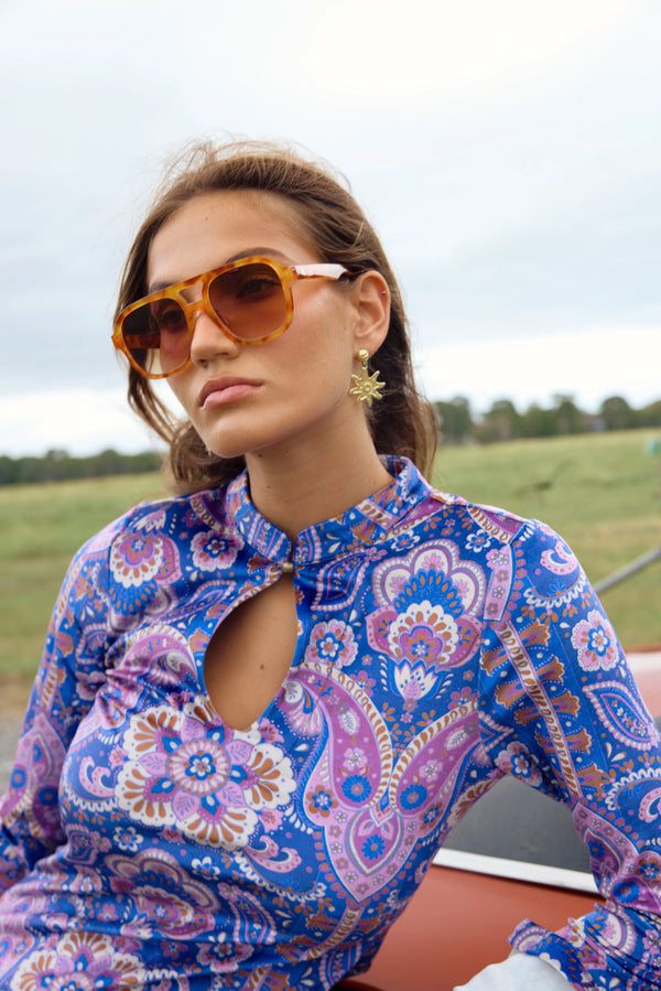 Woman wearing a colorful patterned shirt and sunglasses outdoors.