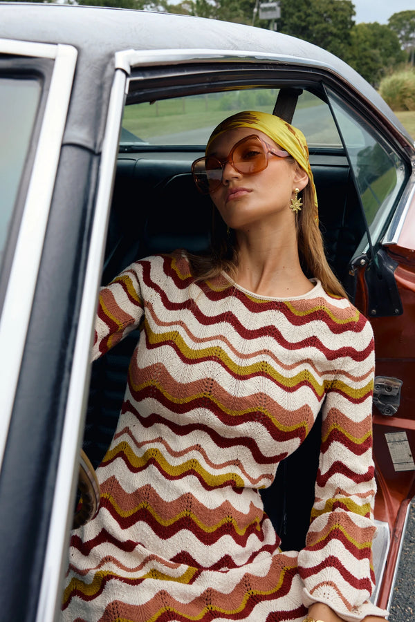 Woman in a patterned dress sitting in a car with an open door.