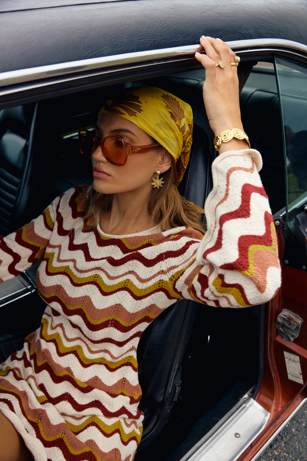 Woman in a patterned sweater and yellow headscarf sitting in a car.