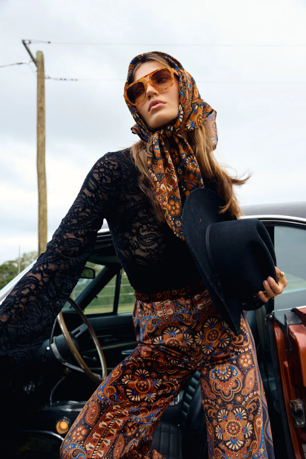 Woman in patterned outfit and scarf standing next to a car outdoors