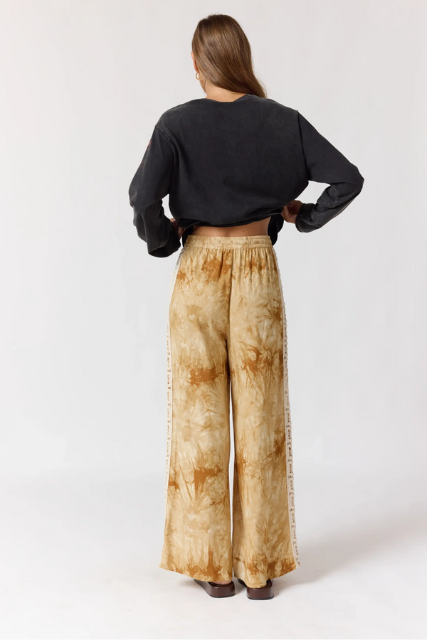 Person wearing a black top and beige tie-dye pants on a white background