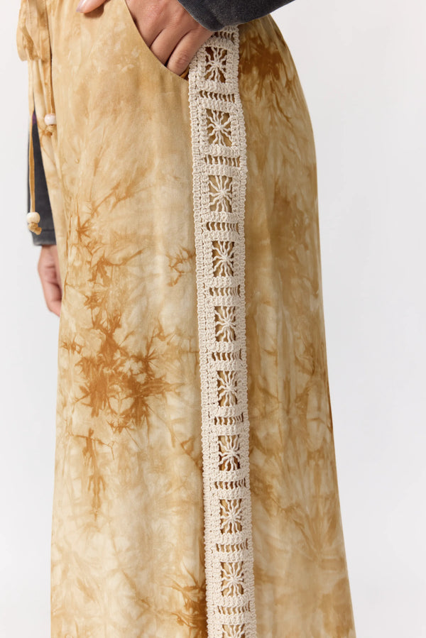 Close-up of a beige tie-dye garment with white lace trim on a plain background