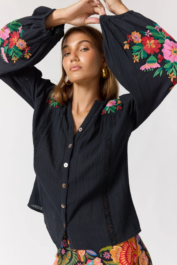 Woman wearing a black blouse with colorful floral embroidery on a white background