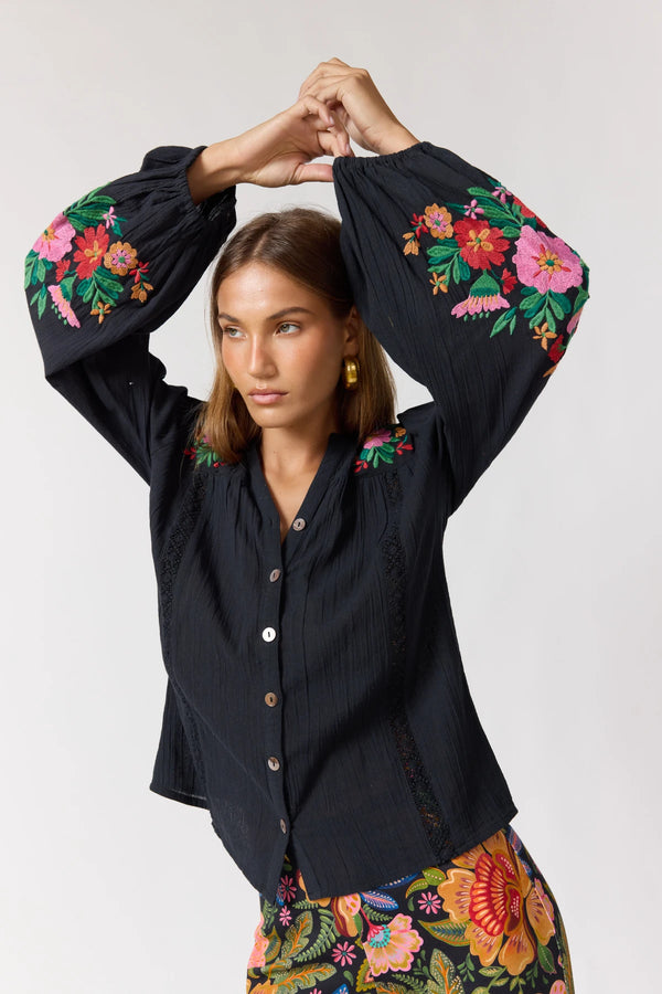 Woman wearing a black blouse with colorful floral embroidery on a white background