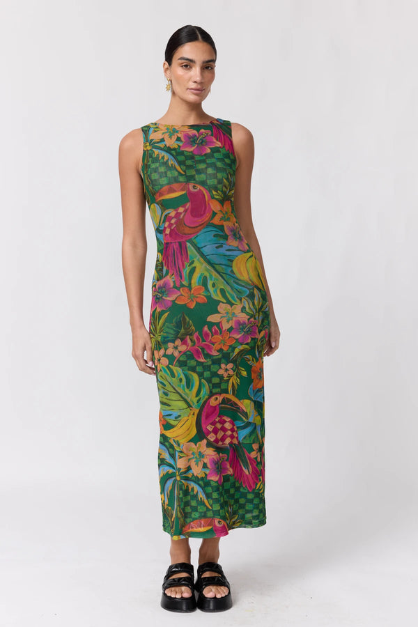 A woman modeling a sleeveless midi dress with a vibrant tropical print featuring green foliage, pink and orange birds, and yellow flowers on a dark green background, paired with black platform sandals against a plain white studio backdrop.
