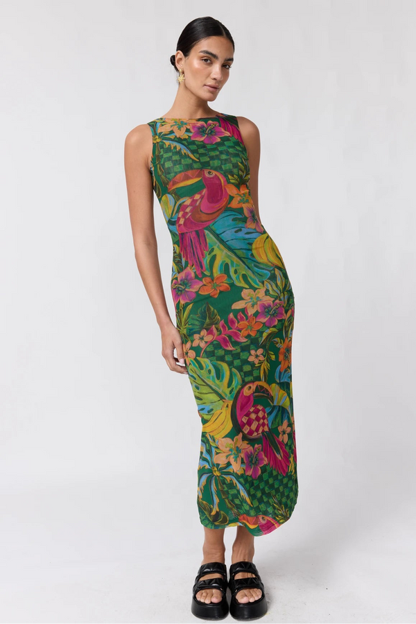 A woman modeling a sleeveless, bodycon maxi dress with a vibrant tropical print featuring green foliage, pink and orange birds, and yellow accents, paired with black platform sandals against a plain white studio background.