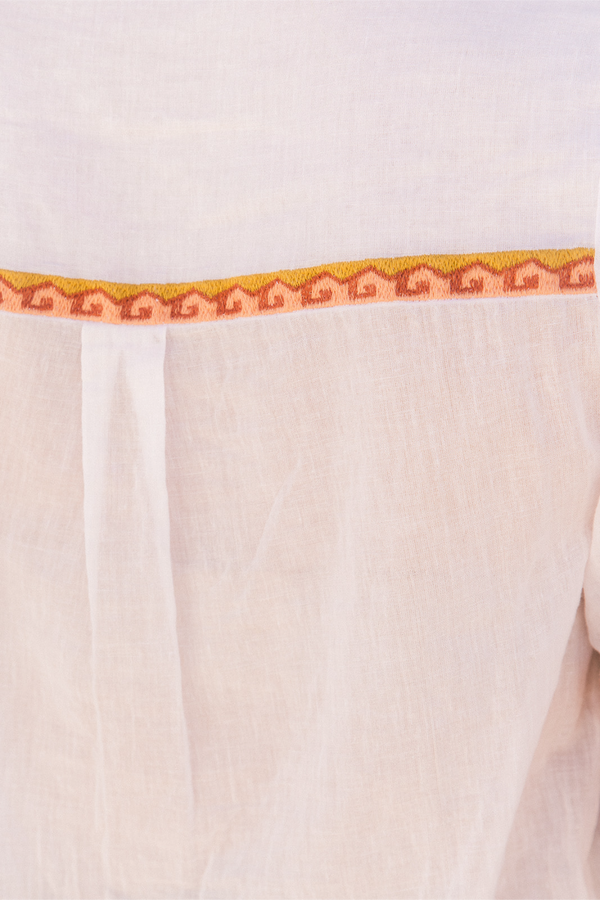 Close-up of a white or off-white fabric garment with a decorative horizontal band featuring a repeating geometric pattern in orange and yellow.