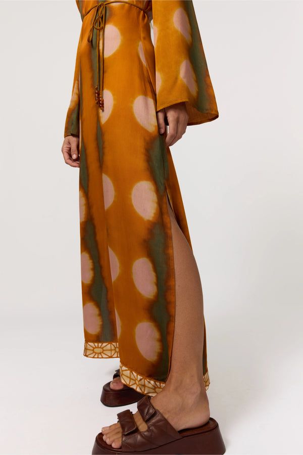 Person wearing a mustard yellow dress with pink polka dots and green accents on a white background