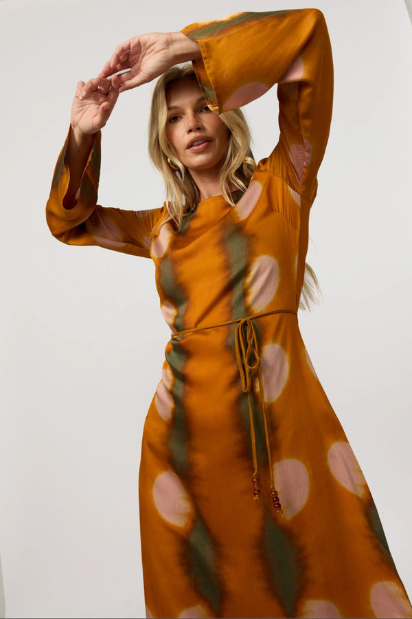 Woman wearing a mustard yellow dress with a pattern, posing against a white background