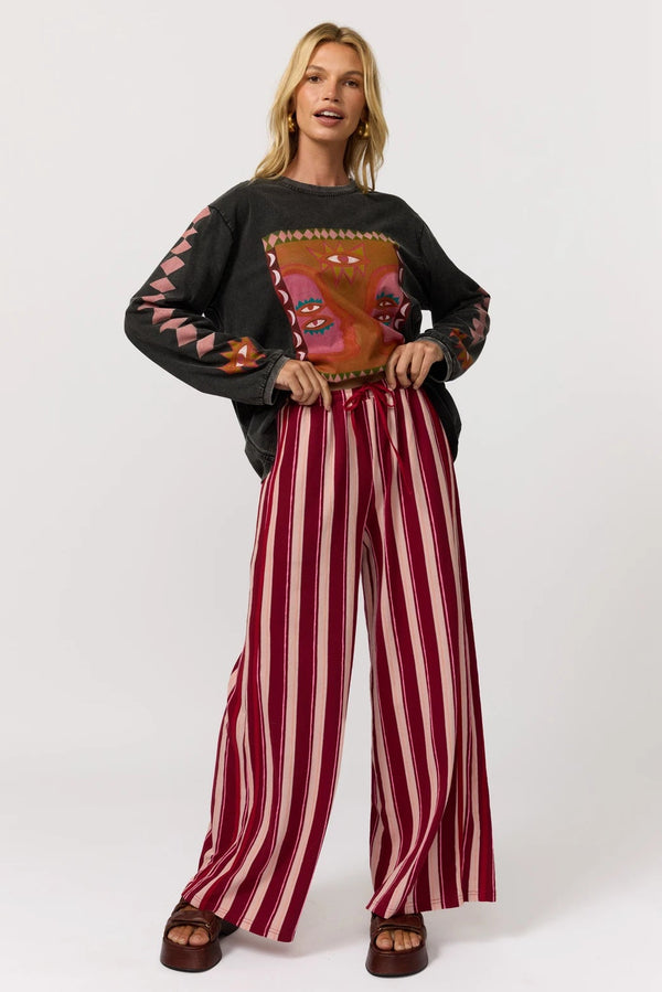 Woman wearing a black sweater with a colorful design and red and white striped pants on a white background
