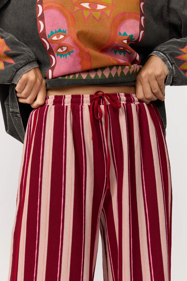 Person wearing a colorful jacket with abstract designs and red and pink striped pants.