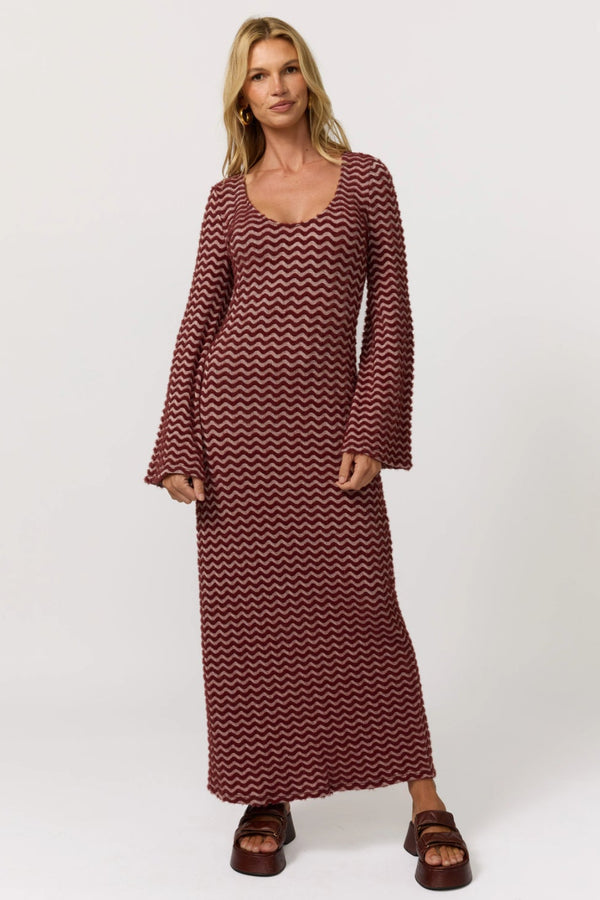 Woman wearing a long burgundy dress with a zigzag pattern on a white background