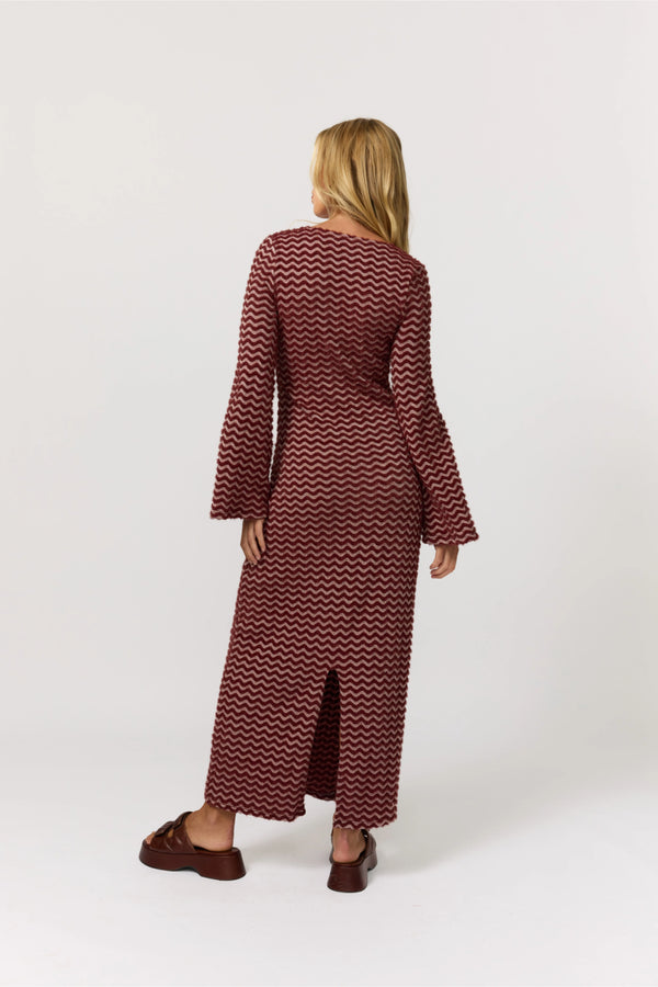 Woman wearing a long burgundy dress with a zigzag pattern on a white background