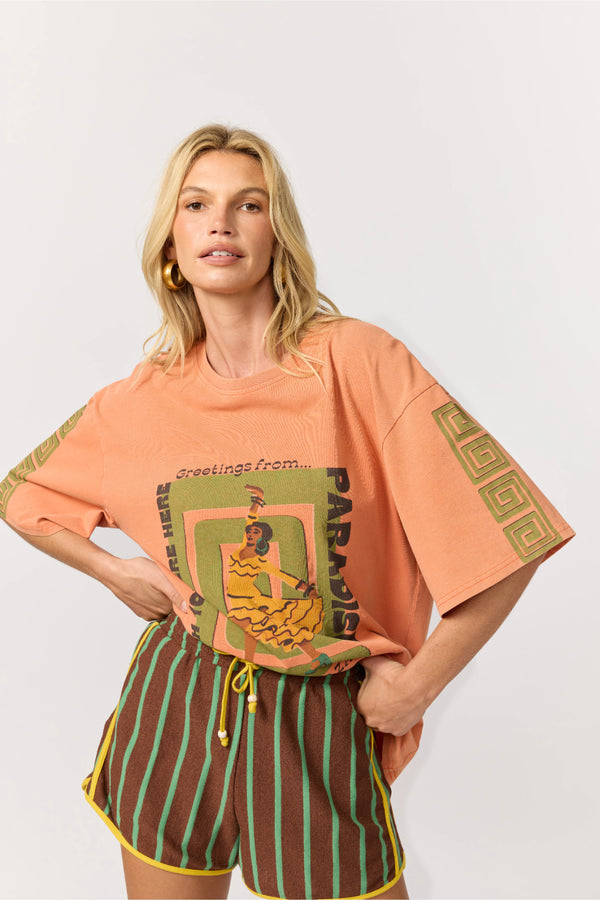 Woman wearing a peach-colored t-shirt with graphic design and striped shorts on a white background