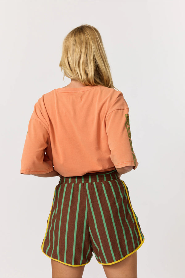 Person wearing an orange top and striped shorts on a white background