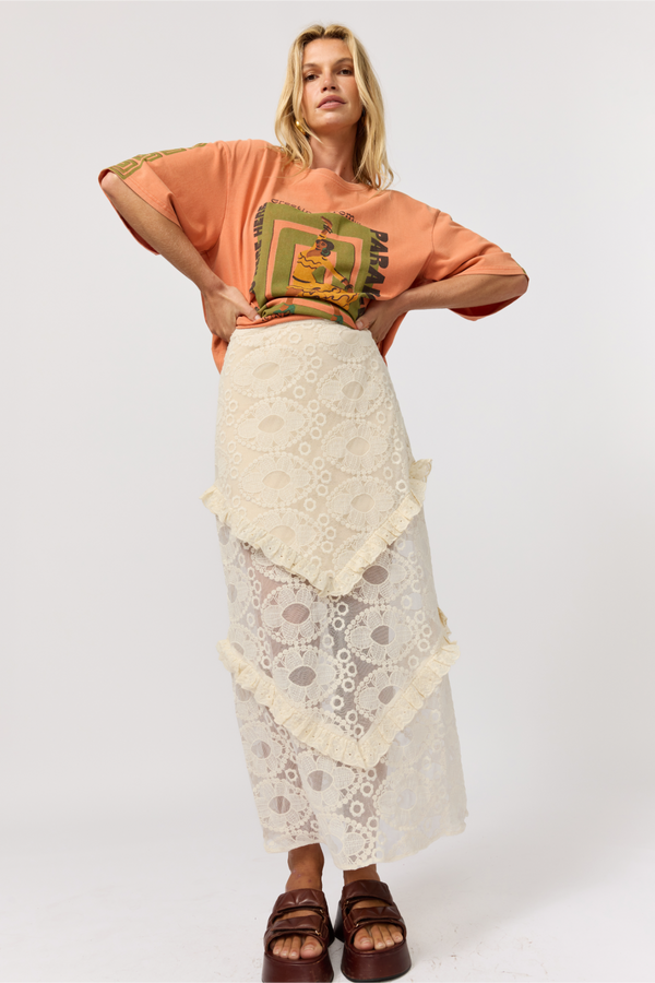 Woman wearing an orange top with a green graphic and a white lace skirt on a white background