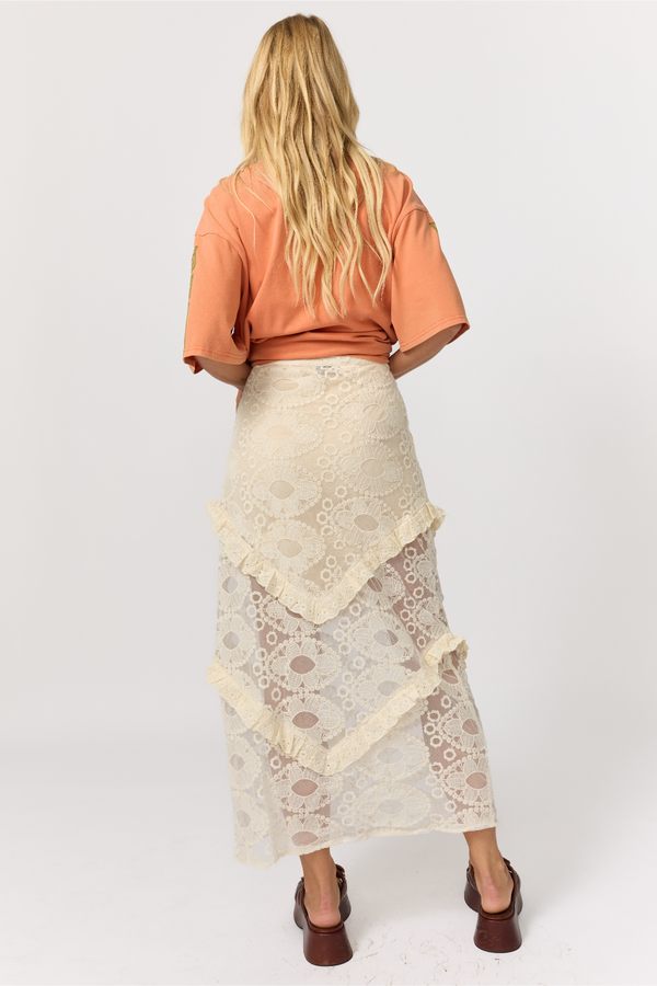Person wearing an orange top and beige lace skirt on a white background