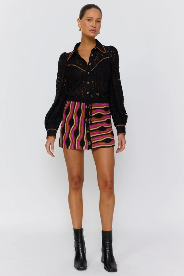 Woman wearing a black jacket, patterned shorts, and black boots on a white background