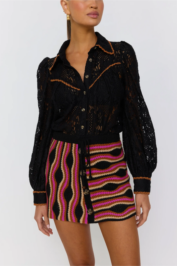 Woman wearing a black patterned top and colorful skirt on a white background