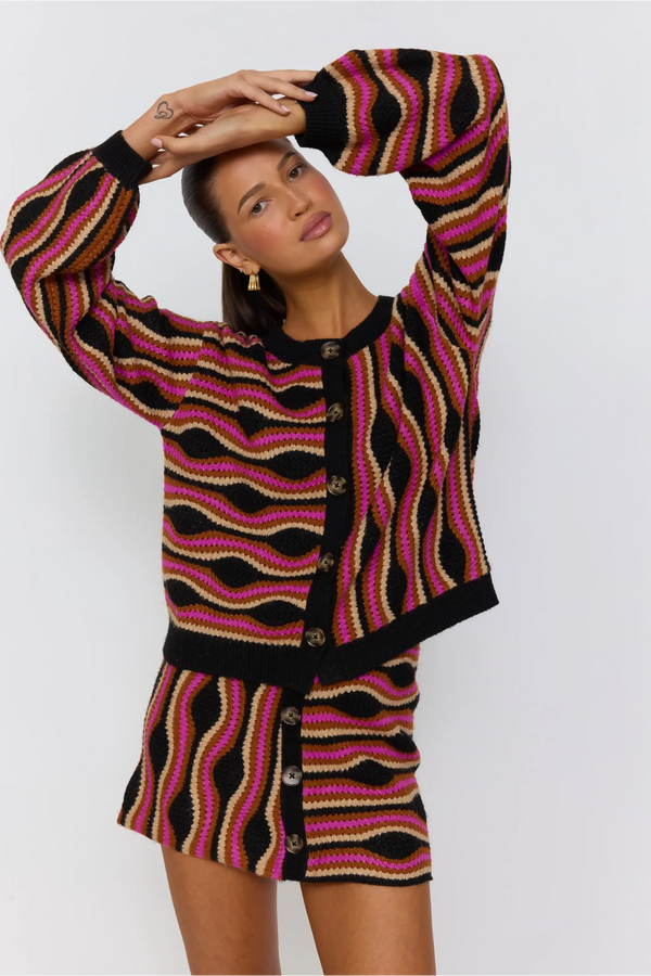 Woman wearing a patterned cardigan and skirt set against a white background