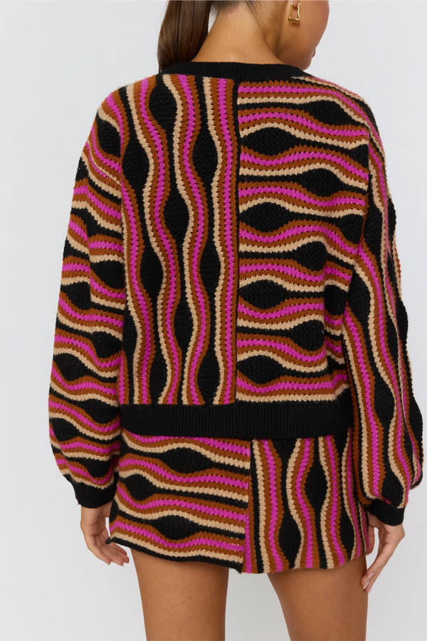 Person wearing a patterned sweater with black, pink, and beige colors on a plain background