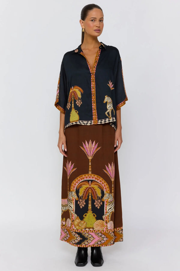 Woman wearing a black top and brown skirt with intricate patterns on a white background