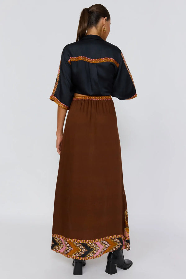 Woman wearing a black top and brown dress with colorful patterns on a white background