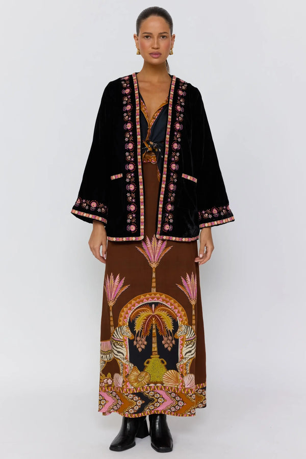 Woman wearing a black embroidered jacket and brown patterned dress on a white background