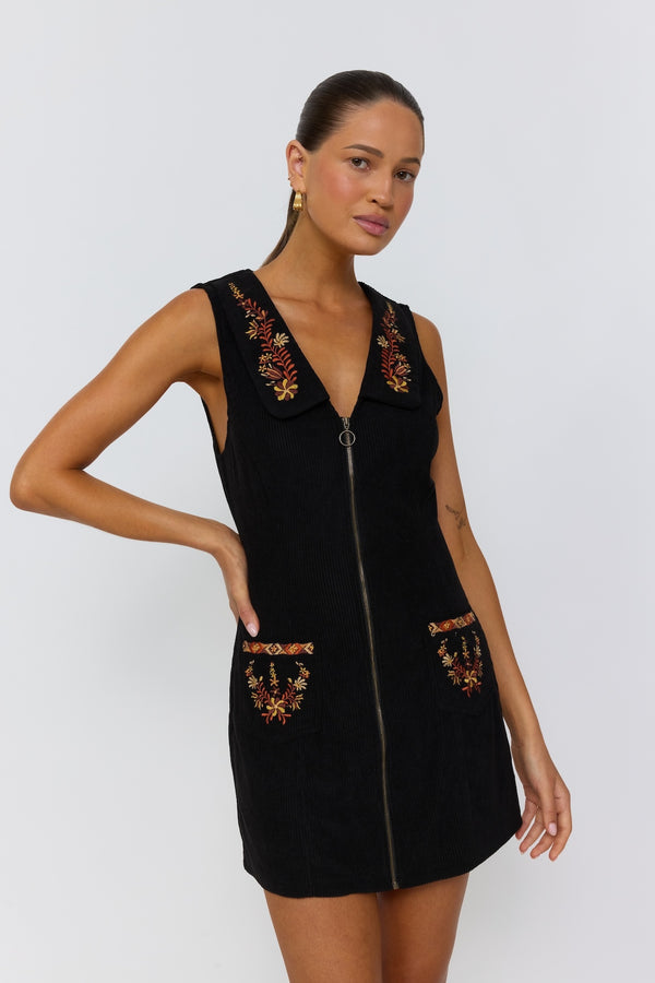 Woman wearing a black dress with floral embroidery on a white background