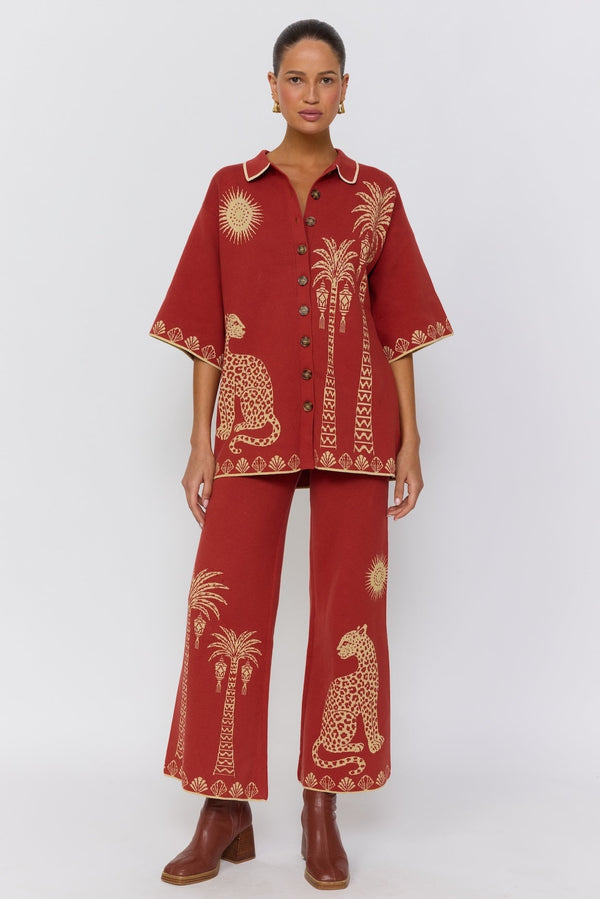 Woman wearing a red embroidered outfit with palm tree and animal designs on a white background