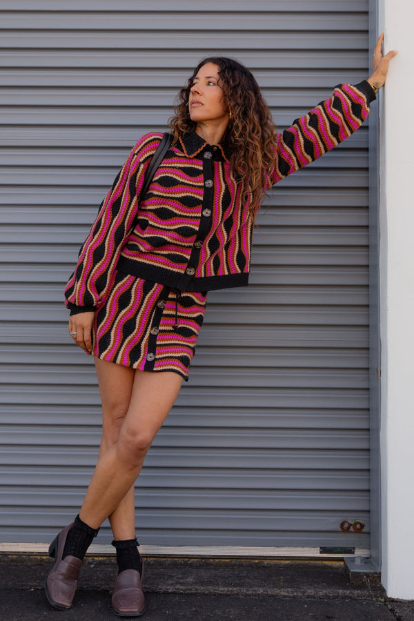 Woman wearing a patterned outfit standing against a gray shutter.