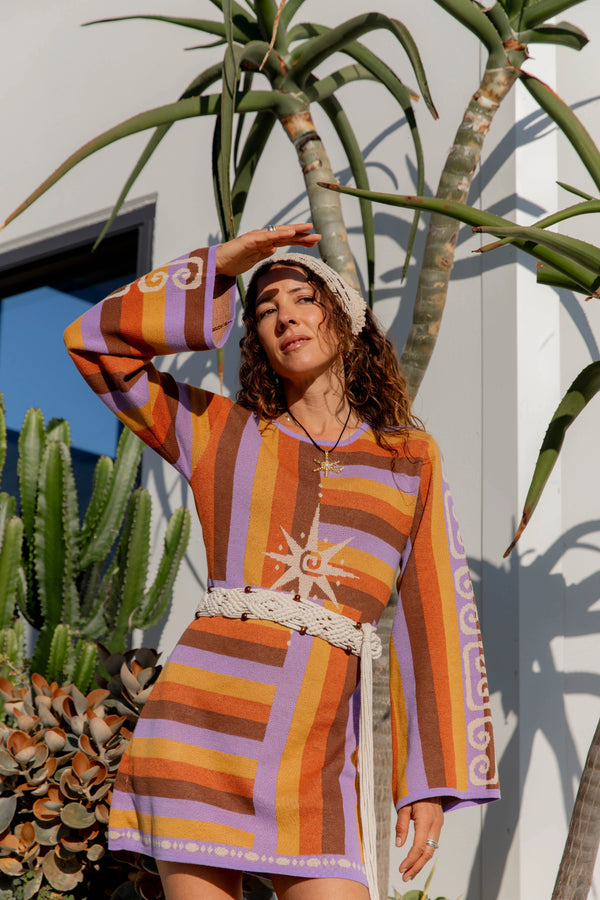 Woman in a colorful striped dress standing under a palm tree with cacti in the background