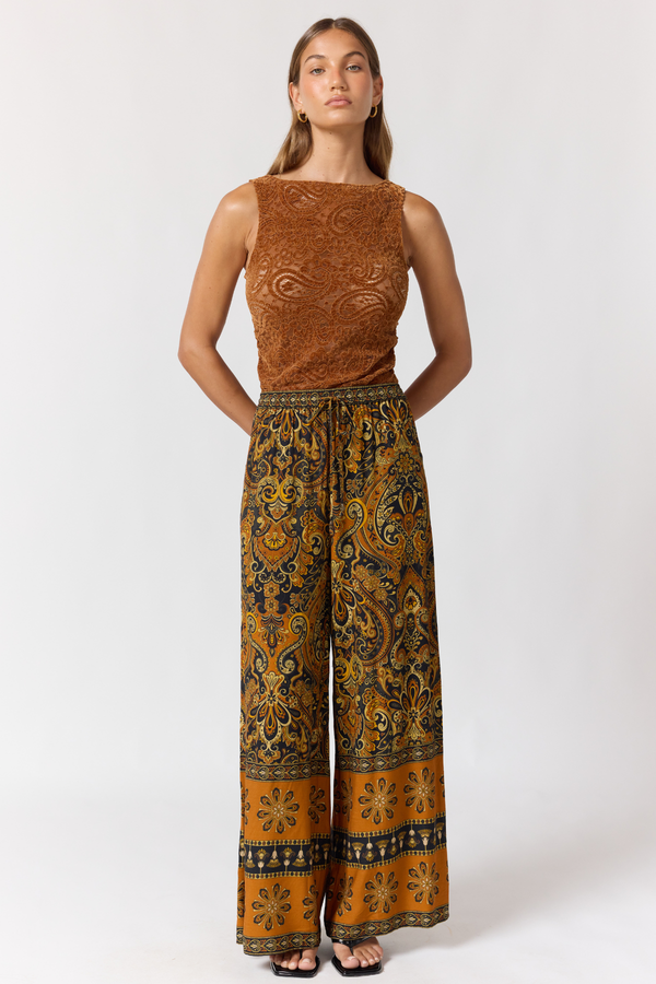 Woman wearing a brown patterned top and wide-leg pants on a white background