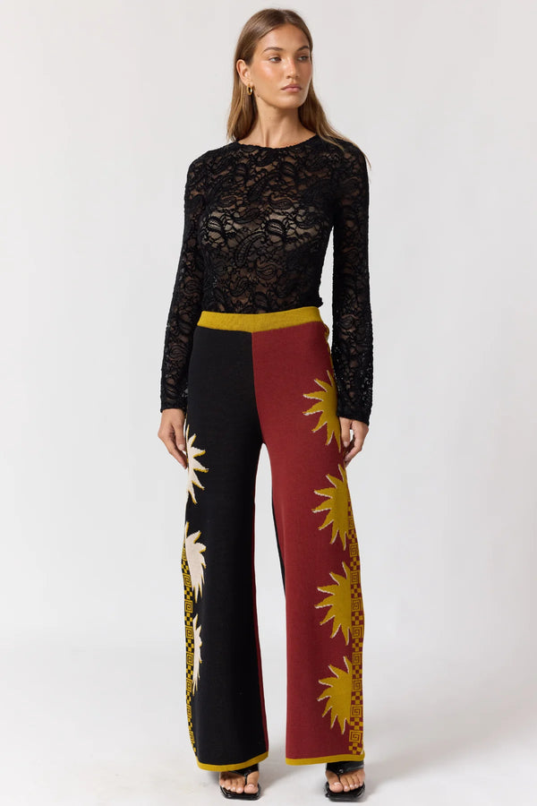 Woman wearing a black lace top and red pants with yellow patterns on a white background