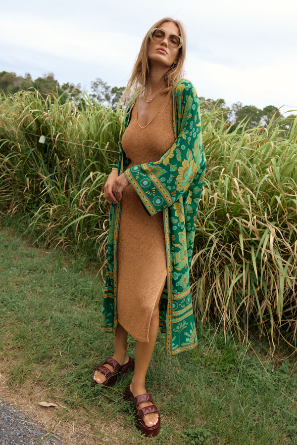Woman in a beige dress and green patterned cover-up standing in tall grass.