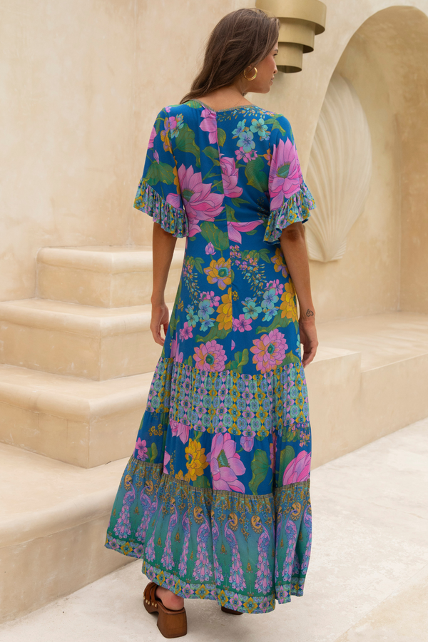 Woman wearing a colorful floral dress standing on stone steps.