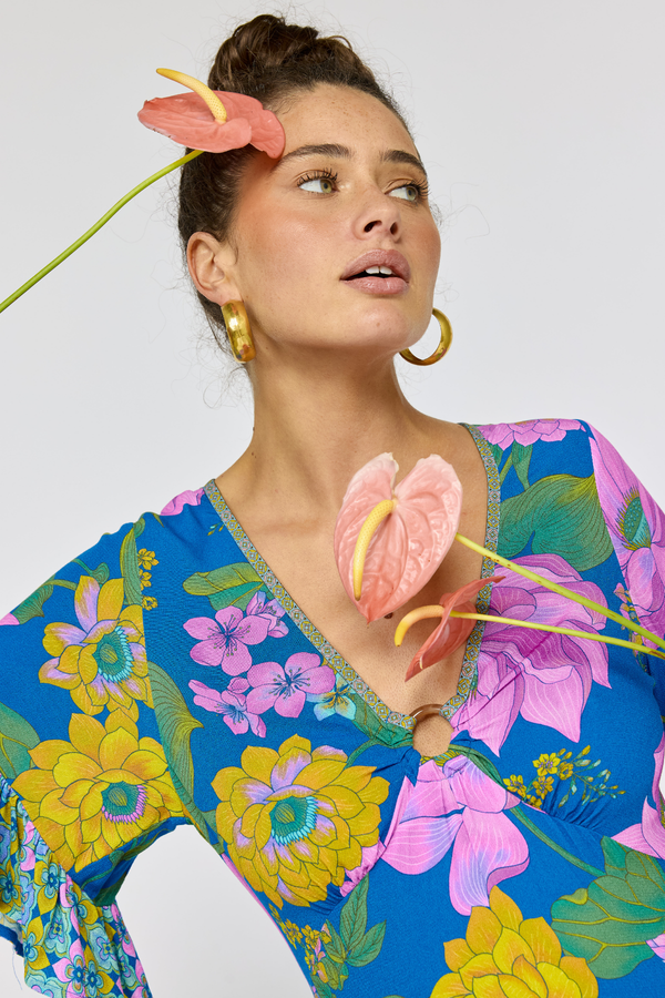 Woman wearing a colorful floral dress with pink flowers in her hair against a white background