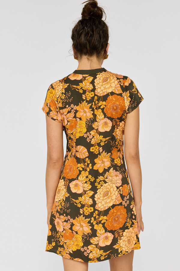 Woman wearing a floral dress with orange and yellow flowers on a plain background