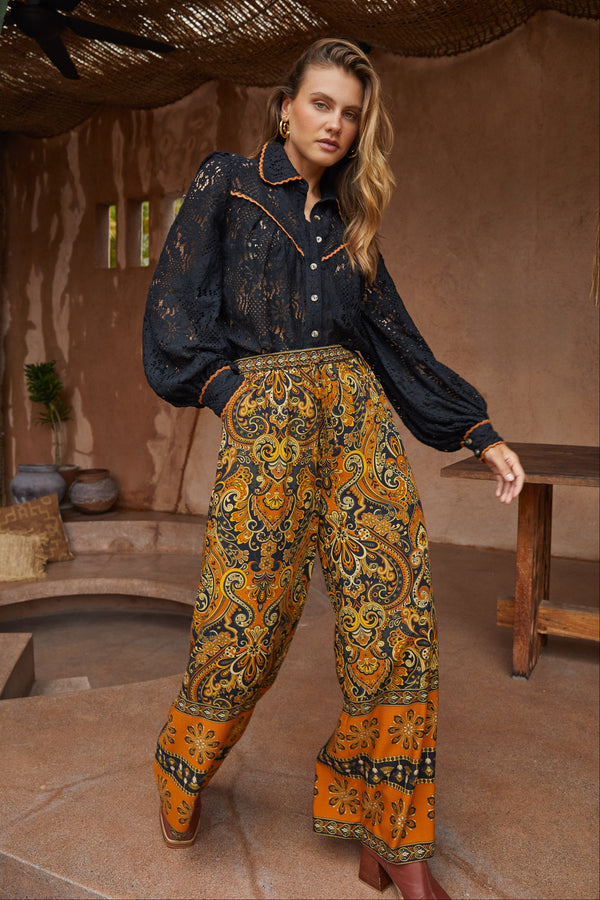 Woman wearing a dark blouse and patterned pants in a rustic setting