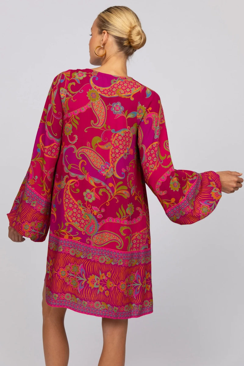 Woman wearing a vibrant pink dress with colorful patterns on a plain background