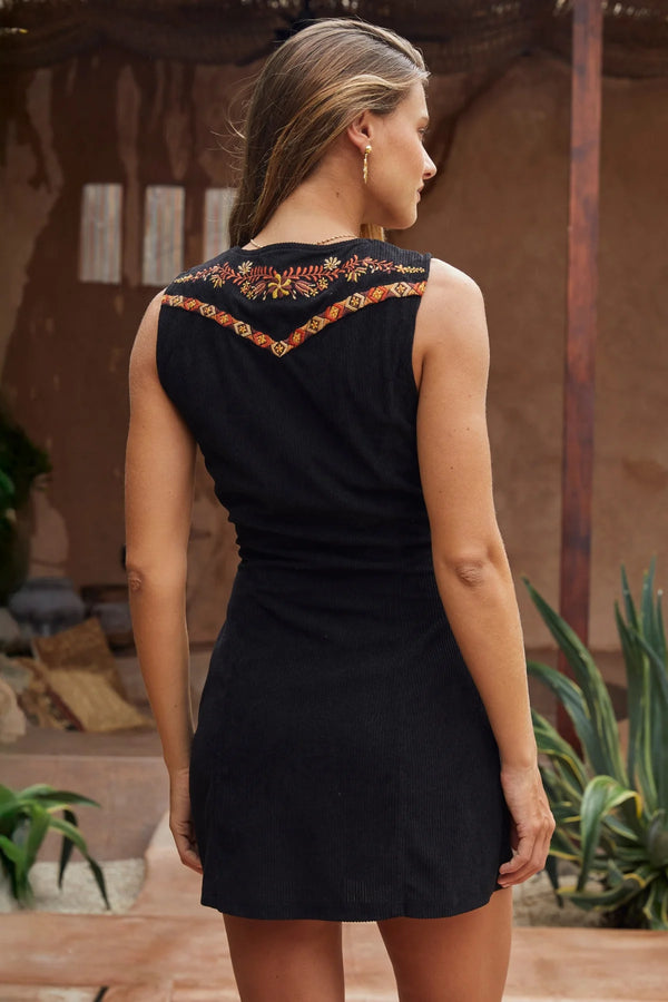 Woman wearing a black dress with floral embroidery in an outdoor setting