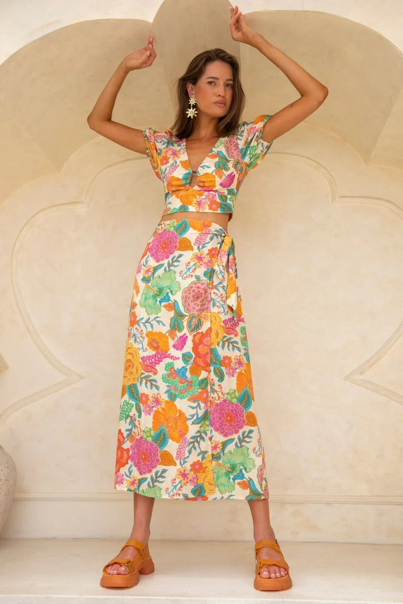 Woman wearing a colorful floral dress against a beige wall.