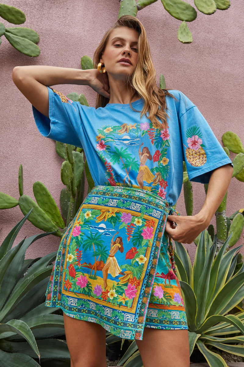 Woman wearing a colorful dress with a tropical design against a pink wall with cacti.