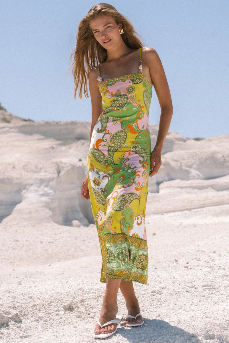 Woman wearing a colorful floral dress standing on a rocky beach.