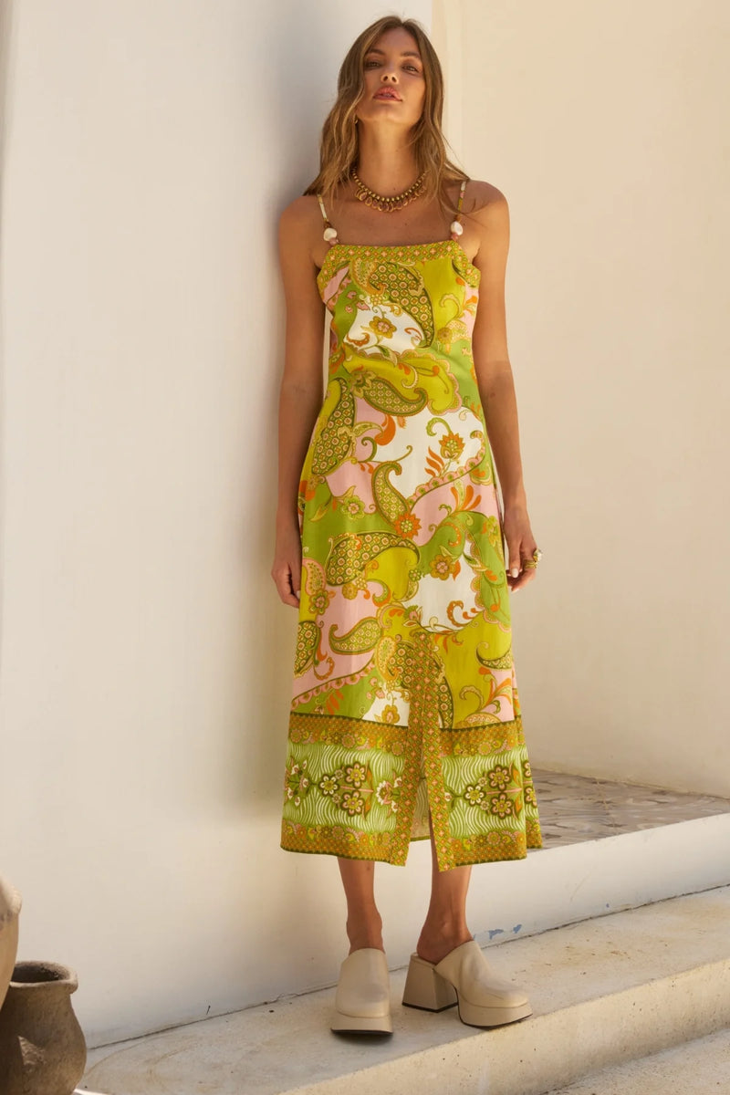 Woman wearing a floral dress standing against a white wall.
