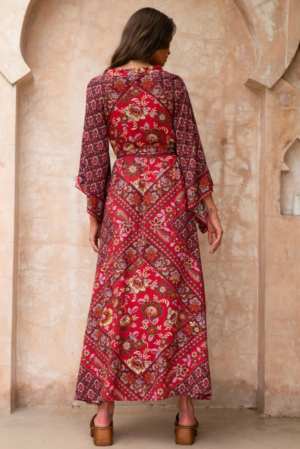 Woman wearing a red patterned dress standing in front of a beige archway.