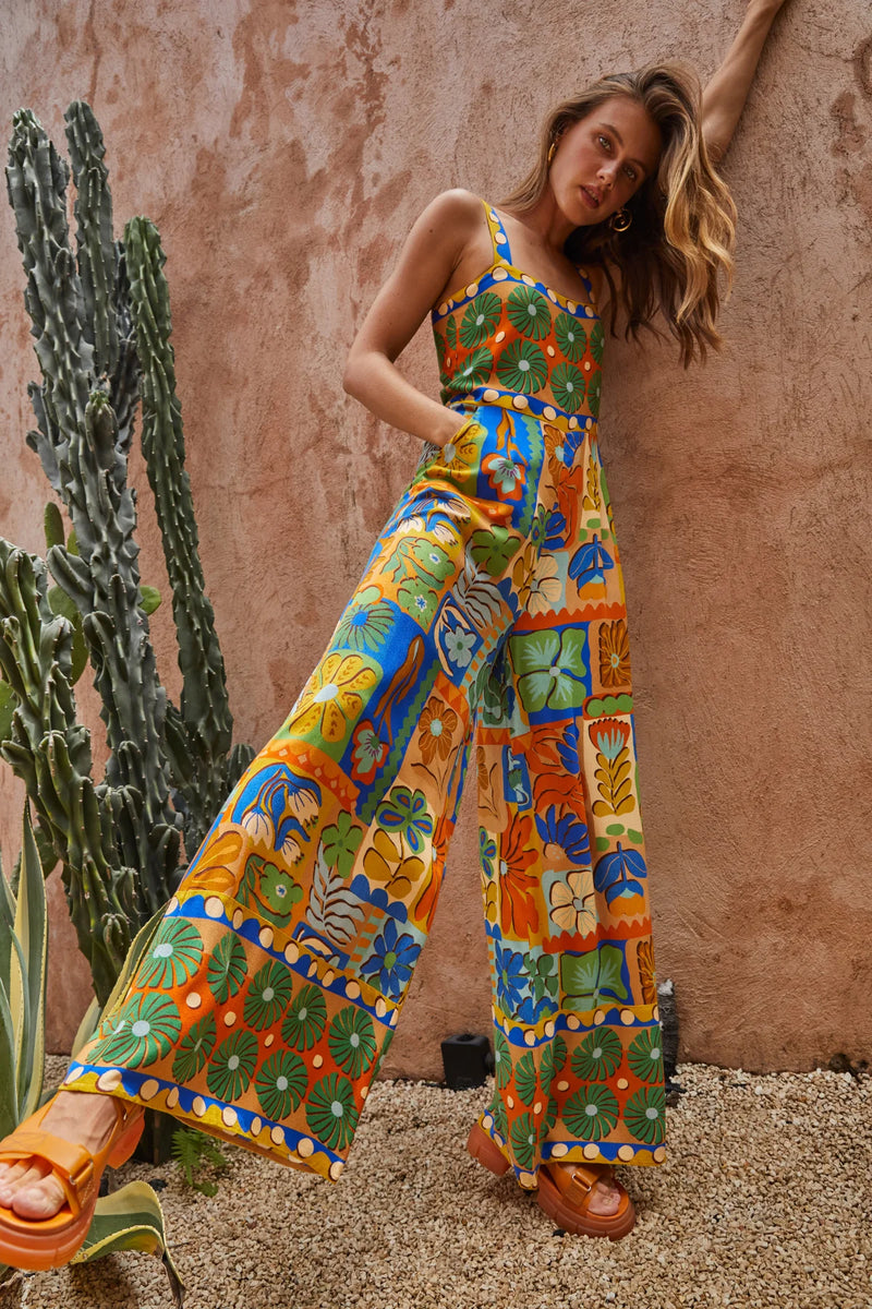 Woman wearing a colorful patterned jumpsuit standing next to a cactus plant.