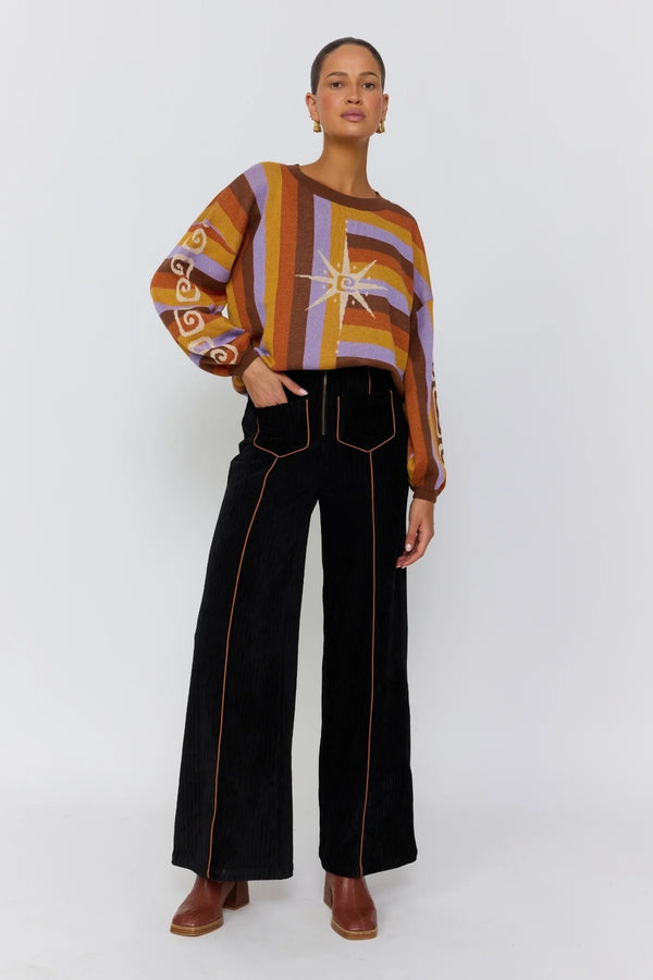 Woman wearing a colorful patterned top and black pants on a white background