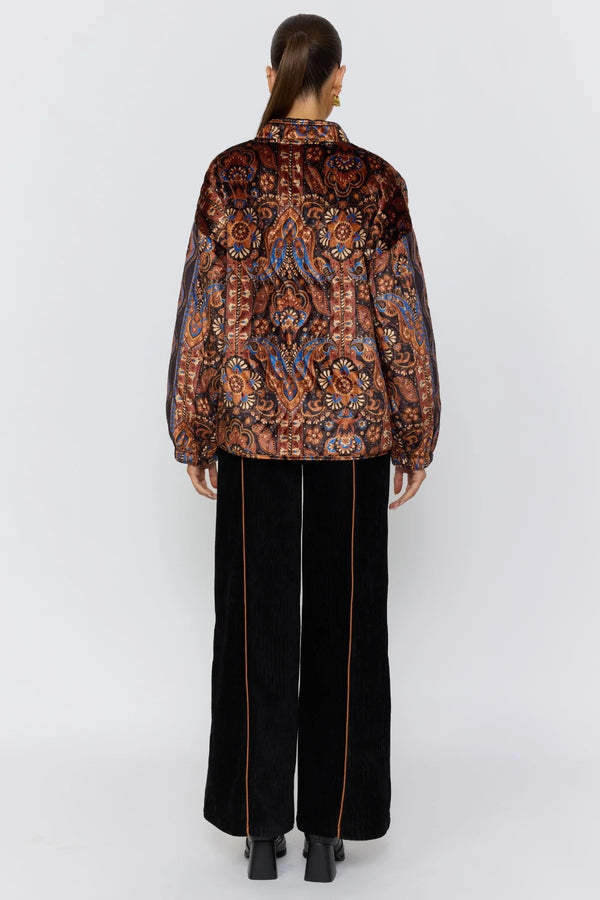 Person wearing a patterned shirt and black pants on a white background