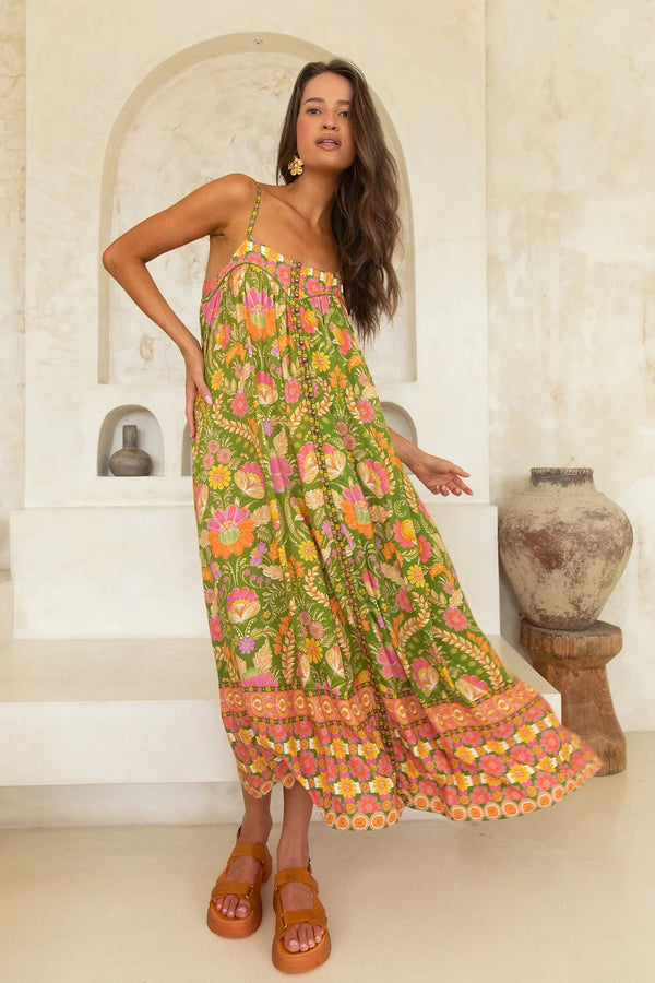 Woman wearing a colorful floral dress standing in a sunlit room with stone walls.